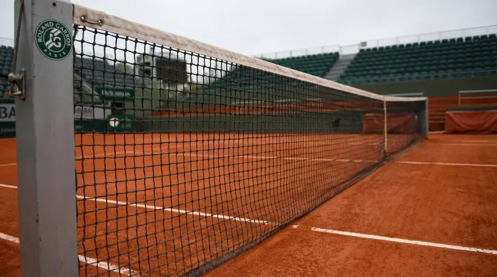 Filet de tennis en gros plan sur un court en terre battue vide avec les lignes blanches nettes sous un ciel couvert