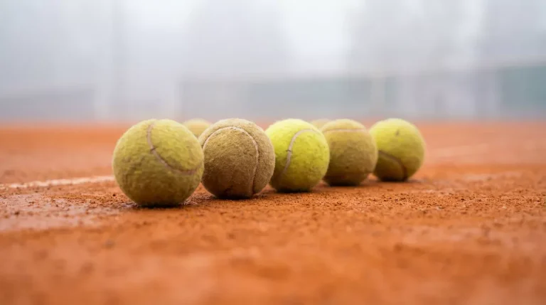 Plusieurs balles de tennis alignées sur une surface en terre battue